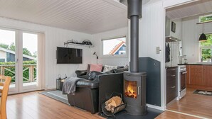 A modern living room with a black wood-burning stove, a leather sofa, and a flat-screen TV. - Holiday Home in Juelsminde (Horsens)