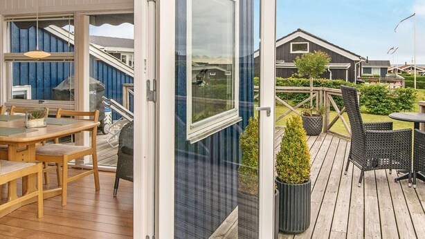 A wooden deck with outdoor furniture, a glass door leading to a covered patio, and a view of neighboring houses. - Holiday Home in Juelsminde (Horsens)