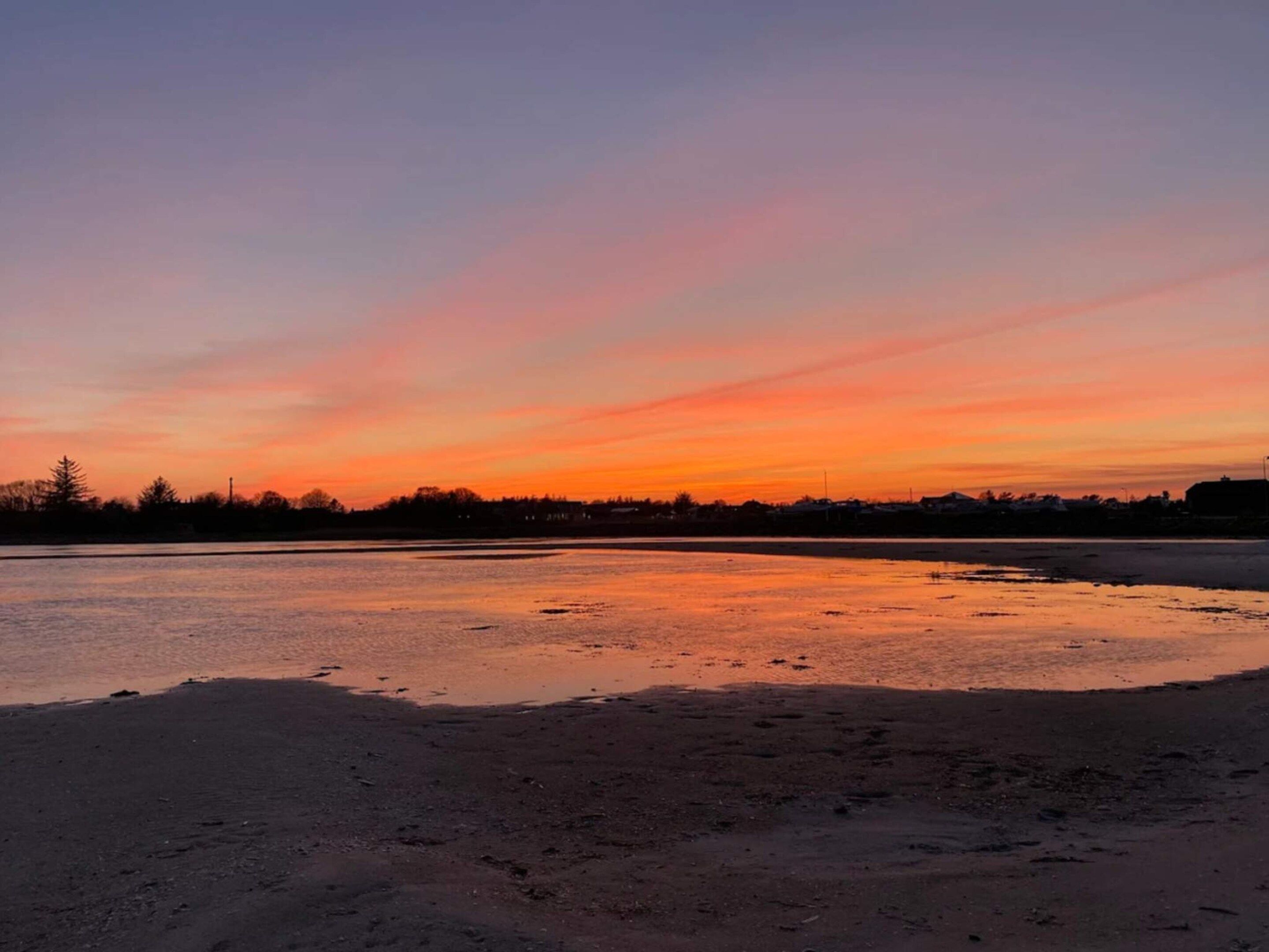 A sunset over a calm body of water with a distant shoreline.
