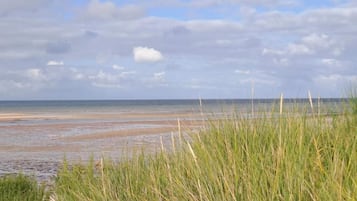 A beach with grassy dunes and a calm sea under a partly cloudy sky.