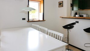 A white dining table with chairs, a floor lamp, a window with blinds, and a kitchen area with cabinets and appliances. - 6 Person Holiday Home in Hadsund (Hadsund)