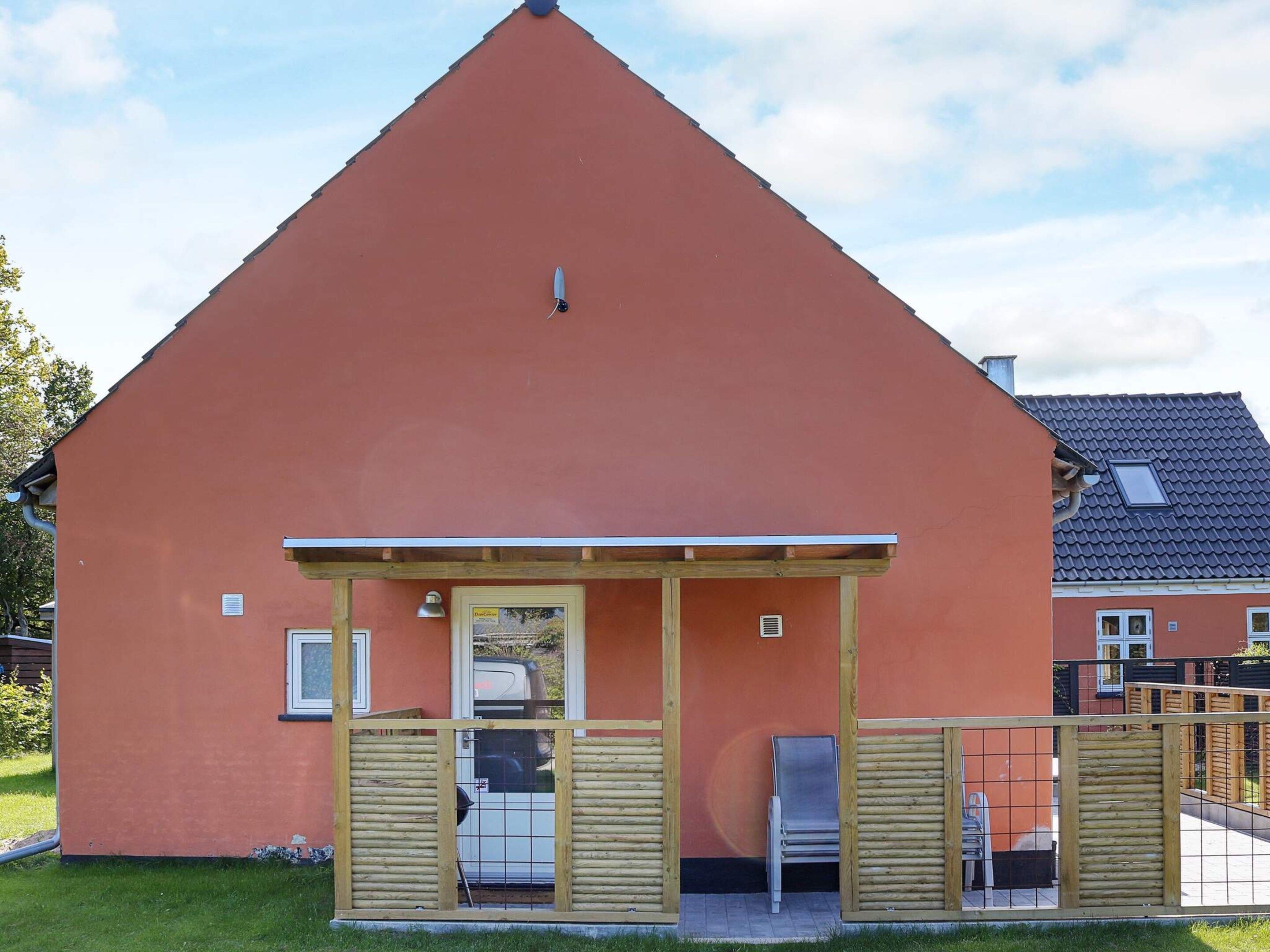 Una edificación de un solo nivel con techo inclinado, un patio cubierto con mesa y sillas, y un ventanal.