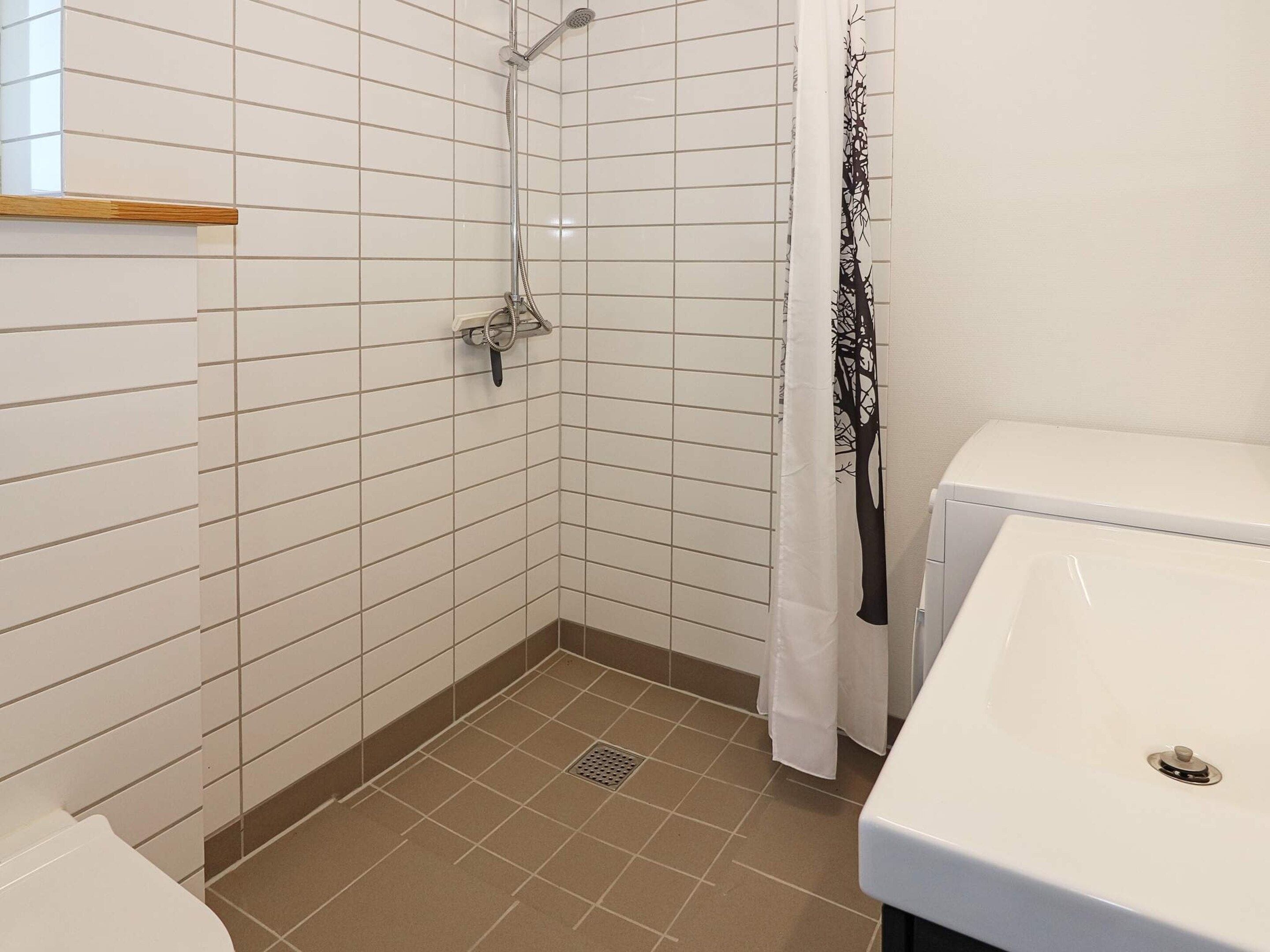 Un baño con paredes de azulejos blancos, ducha, inodoro y lavamanos.