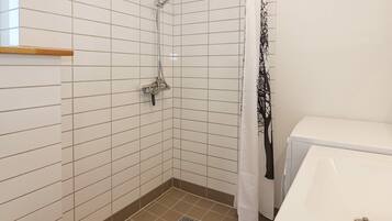 Un baño con paredes de azulejos blancos, ducha, inodoro y lavamanos.
