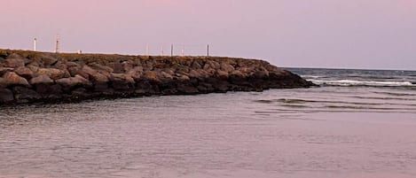 A rocky shoreline with a breakwater and a lighthouse in the distance.