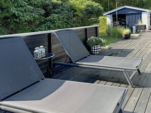 A deck with two lounge chairs, a small table with lanterns, and a shed in the background.