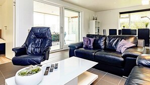 A modern living room with a leather armchair, a black leather sofa, a white coffee table, and a glass door leading to a balcony. - 8 Person Holiday Home in Vaeggerlose (Vaeggerlose)