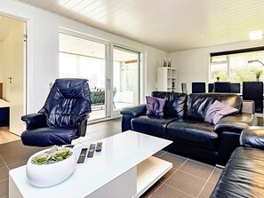 A modern living room with a leather armchair, a black leather sofa, a white coffee table, and a glass door leading to a balcony. - 8 Person Holiday Home in Vaeggerlose (Vaeggerlose)