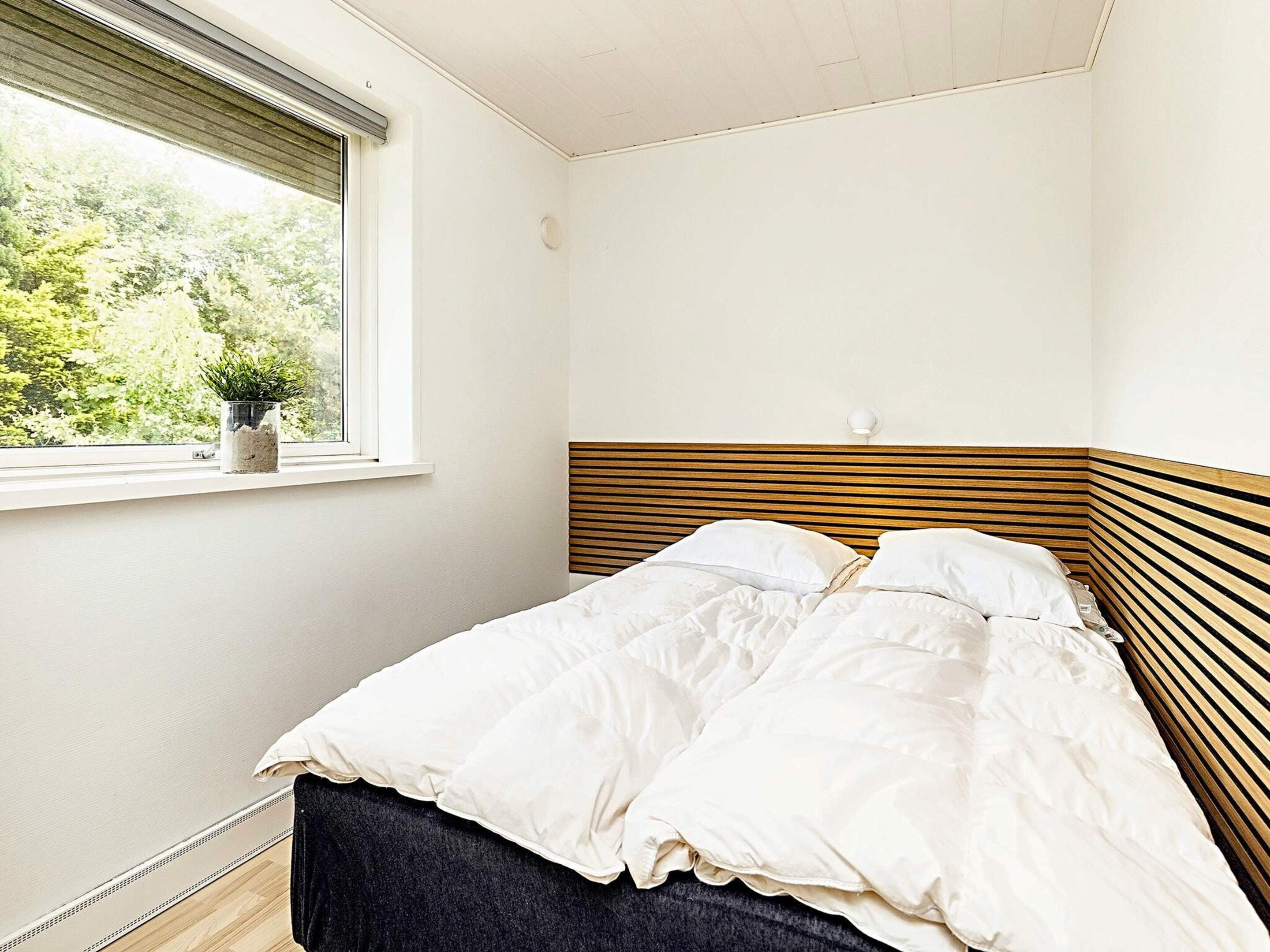 Une chambre à coucher avec un lit, une fenêtre donnant sur un paysage verdoyant et un luminaire fixé au mur.