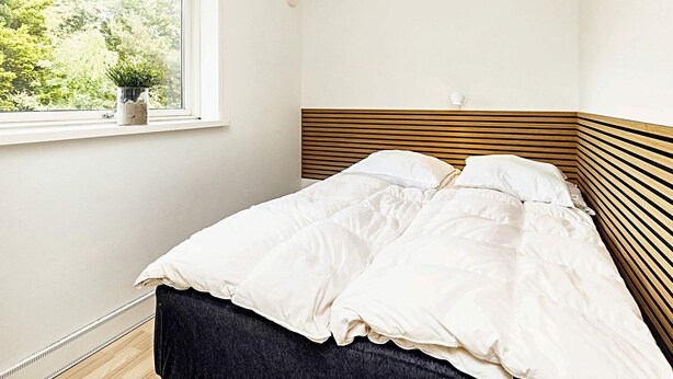 A bedroom with a bed, a window with a view of greenery, and a wall-mounted light fixture. - 8 Person Holiday Home in Vaeggerlose (Vaeggerlose)