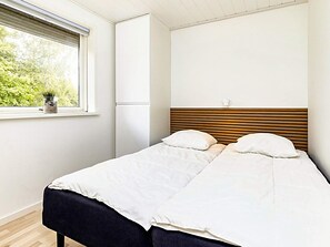 A bedroom with a bed, a window with a view of greenery, and a wall-mounted light fixture.