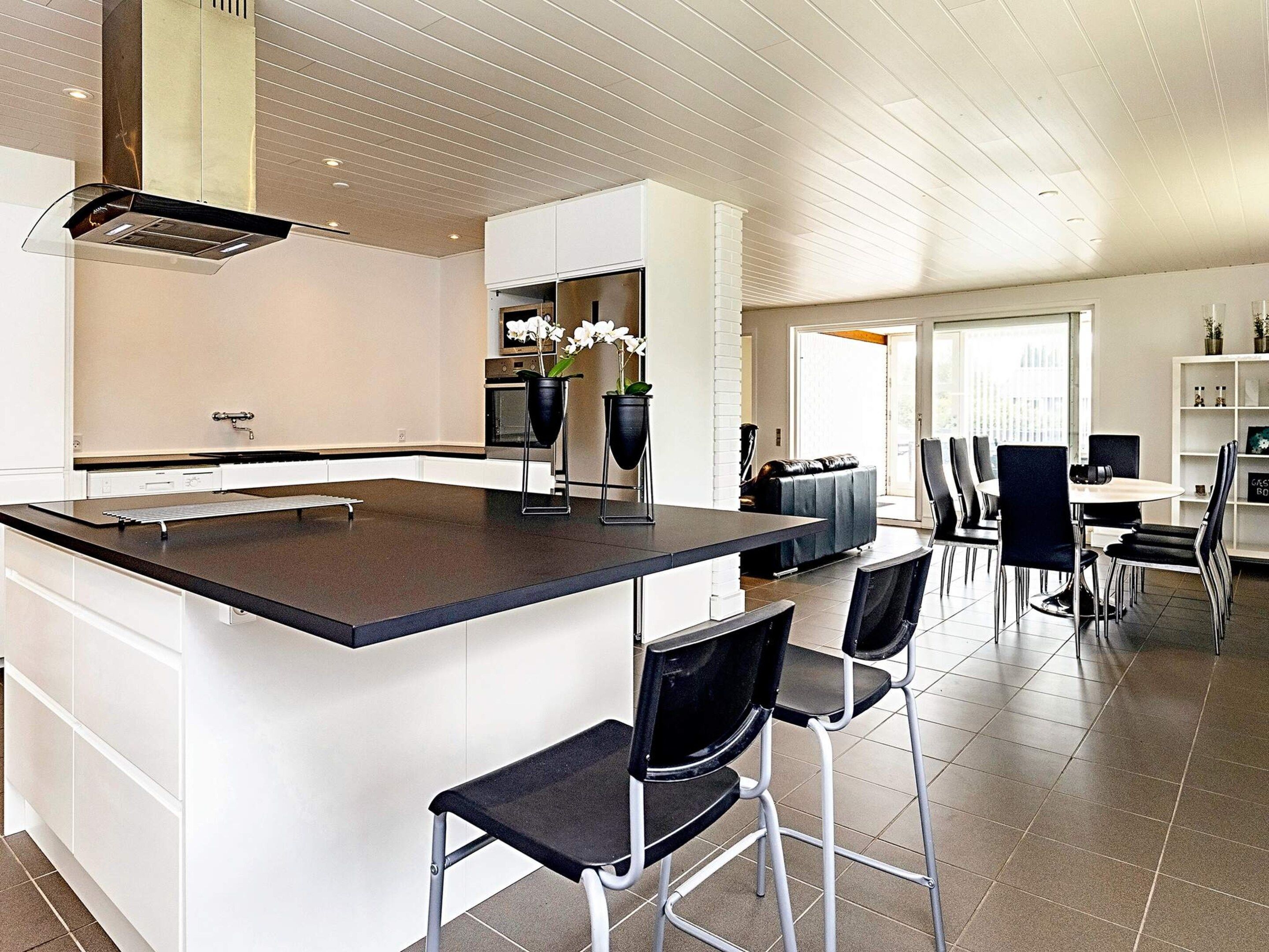 A modern kitchen with a central island, bar stools, and a dining area with chairs.