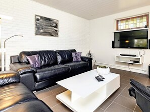 A modern living room with a black leather sofa, white coffee table, and a mounted TV.