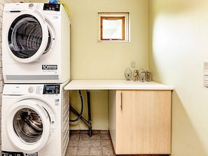 A laundry area with two stacked front-loading washing machines, a small window, and a wooden cabinet. - 8 Person Holiday Home in Vaeggerlose (Vaeggerlose)
