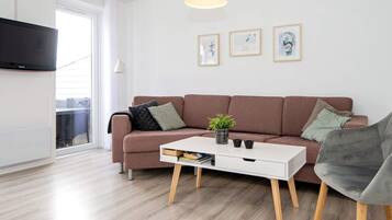 A modern living room with a sofa, a coffee table, and a grey armchair. There are framed artworks on the wall and a potted plant on the coffee table.