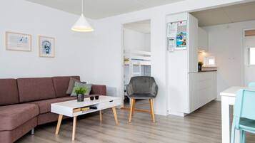 A modern living space with a sofa, a coffee table, a dining area with a chair, and a kitchen area.
