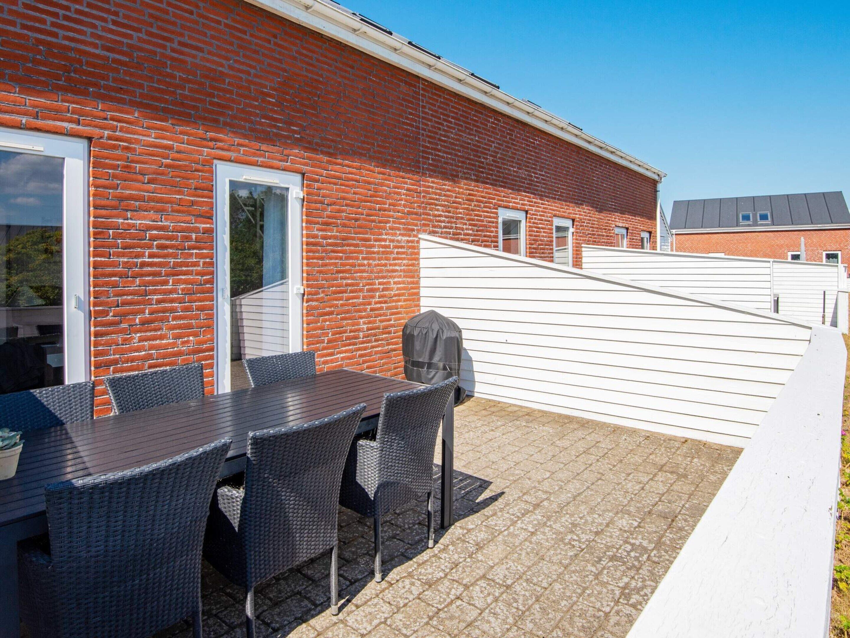An outdoor patio with a brick wall, a covered table, and chairs.