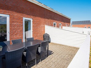 En udendørs terrasse med en murstensvæg, et overdækket bord og stole.