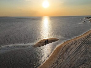 A vast, flat landscape with a single person walking along a narrow path beside a large body of water.
