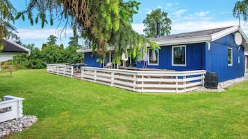 A blue house with a deck, surrounded by a grassy yard and trees.