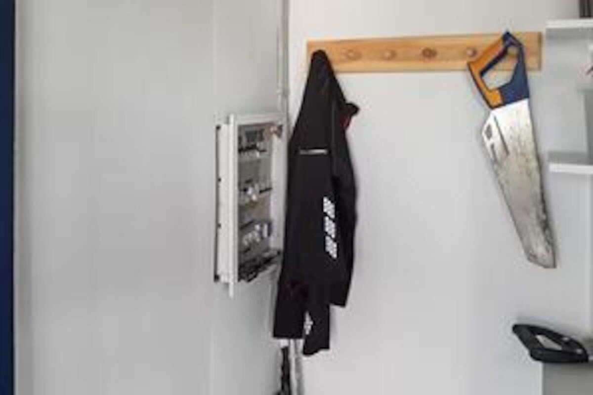 A room with a white wall, a wooden shelf, a black jacket hanging on the wall, and a white door.