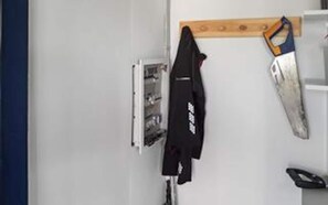 A room with a white wall, a wooden shelf, a black jacket hanging on the wall, and a white door. - Holiday Home in Sydals (Sydals)