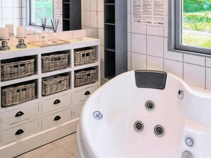 Un baño moderno con una bañera blanca, cestos de mimbre en un mueble y un ventanal con vistas a la vegetación.