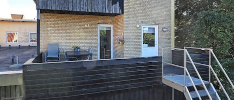 A rooftop terrace with a table and chairs, a small door, and a staircase leading to an upper level.