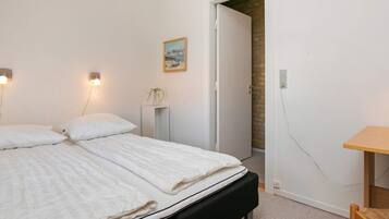 Ein Schlafzimmer mit einem Bett, Nachttischlampen, einem kleinen Tisch und einer Tür zu einem anderen Raum.