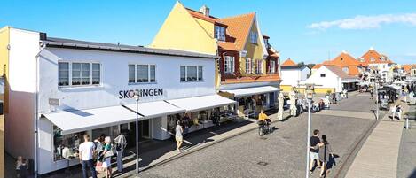 A cobblestone square with shops, a white building with 'SKØTINGEN' signage, and a yellow building with a red roof.