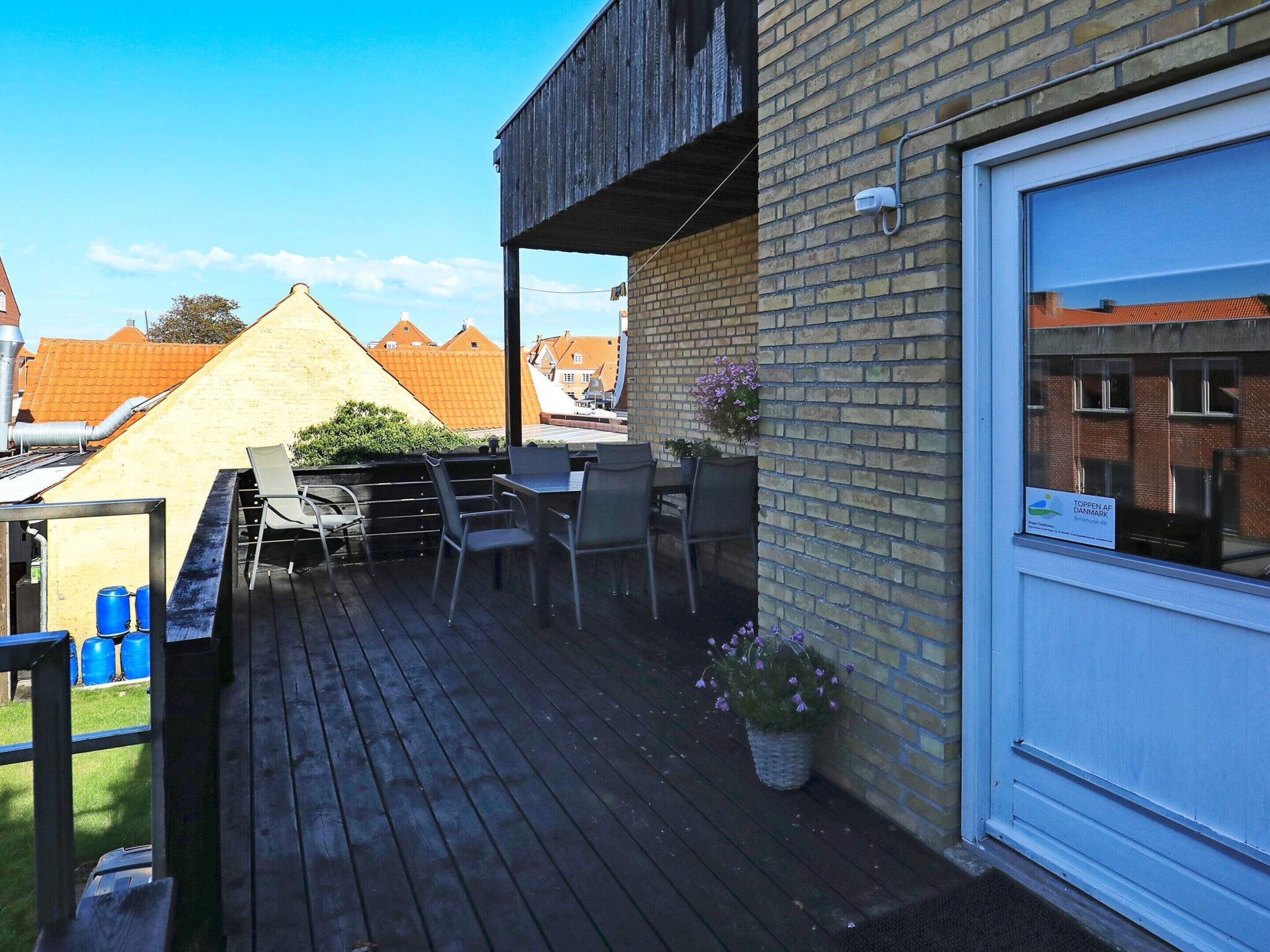 Una terraza de madera con mobiliario exterior, un muro de ladrillo y una ventana con un letrero.