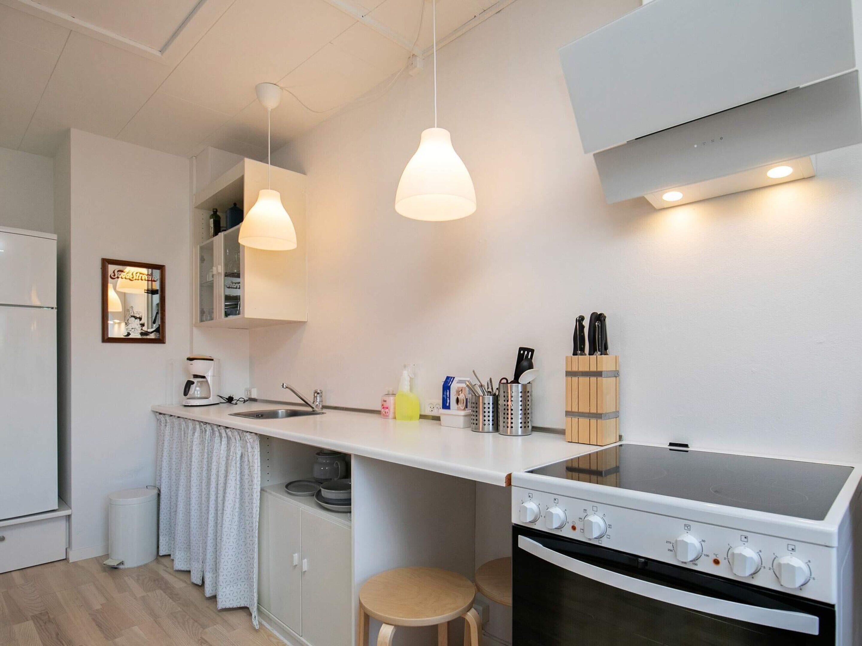 A compact kitchen with a stove, sink, and hanging pendant lights.
