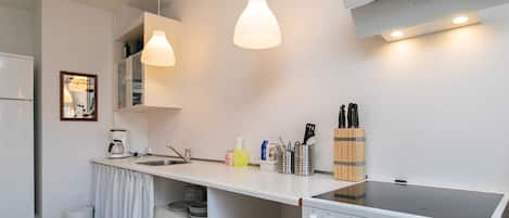 A compact kitchen with a stove, sink, and hanging pendant lights.