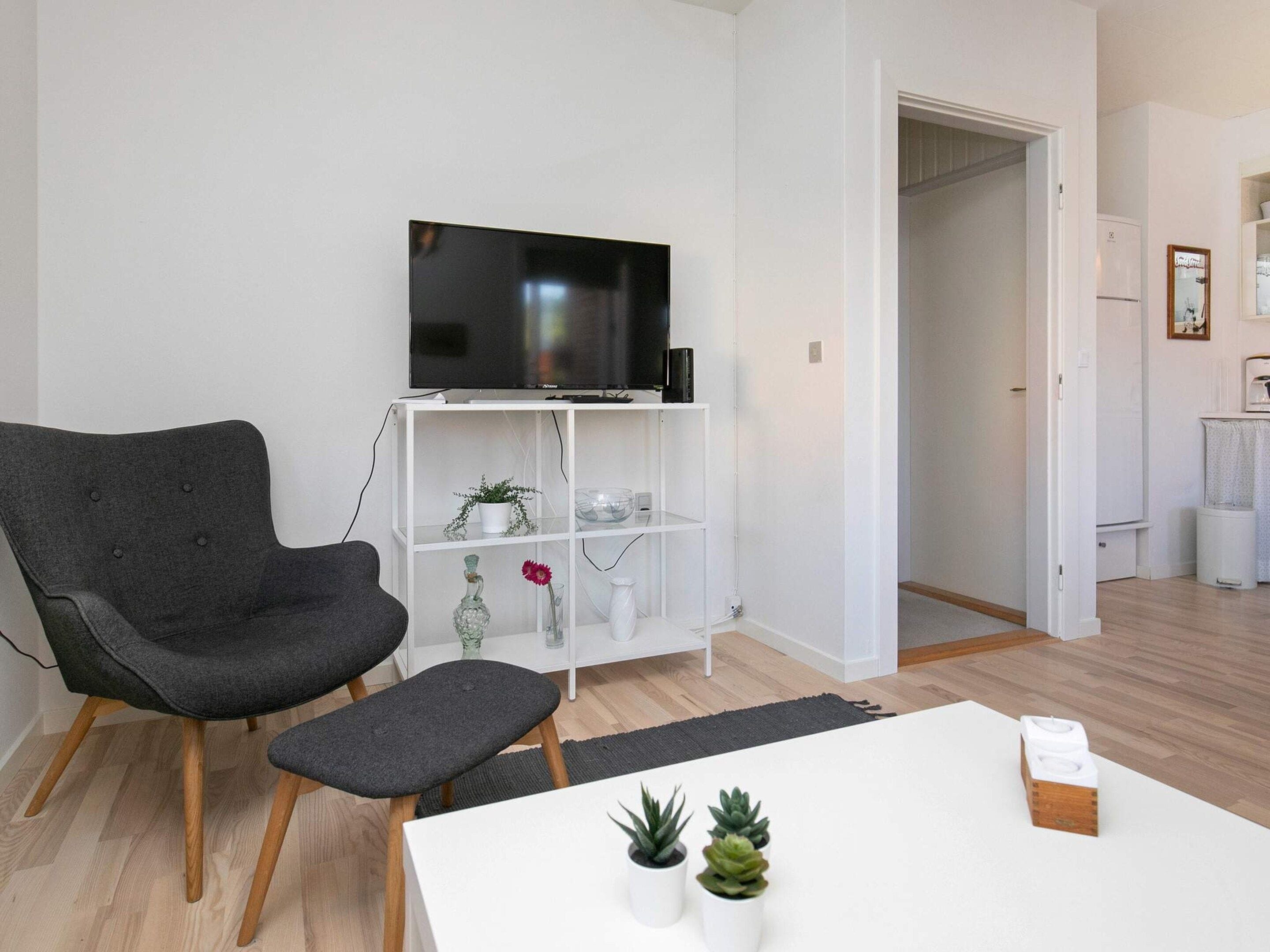 Ein modernes Wohnzimmer mit einem grauen Sessel, einer weißen TV-Konsole und einem kleinen Tisch mit Pflanzen.