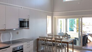 A modern kitchen with white cabinetry, a built-in oven, and a microwave. There is a dining area with a table and chairs, and a sliding glass door leading to an outdoor area. - 6 Person Holiday Home in Dyrvik (Frøya)
