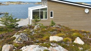 A modern wooden building with a glass extension, situated on a rocky shoreline with a view of the sea. - 6 Person Holiday Home in Dyrvik (Frøya)