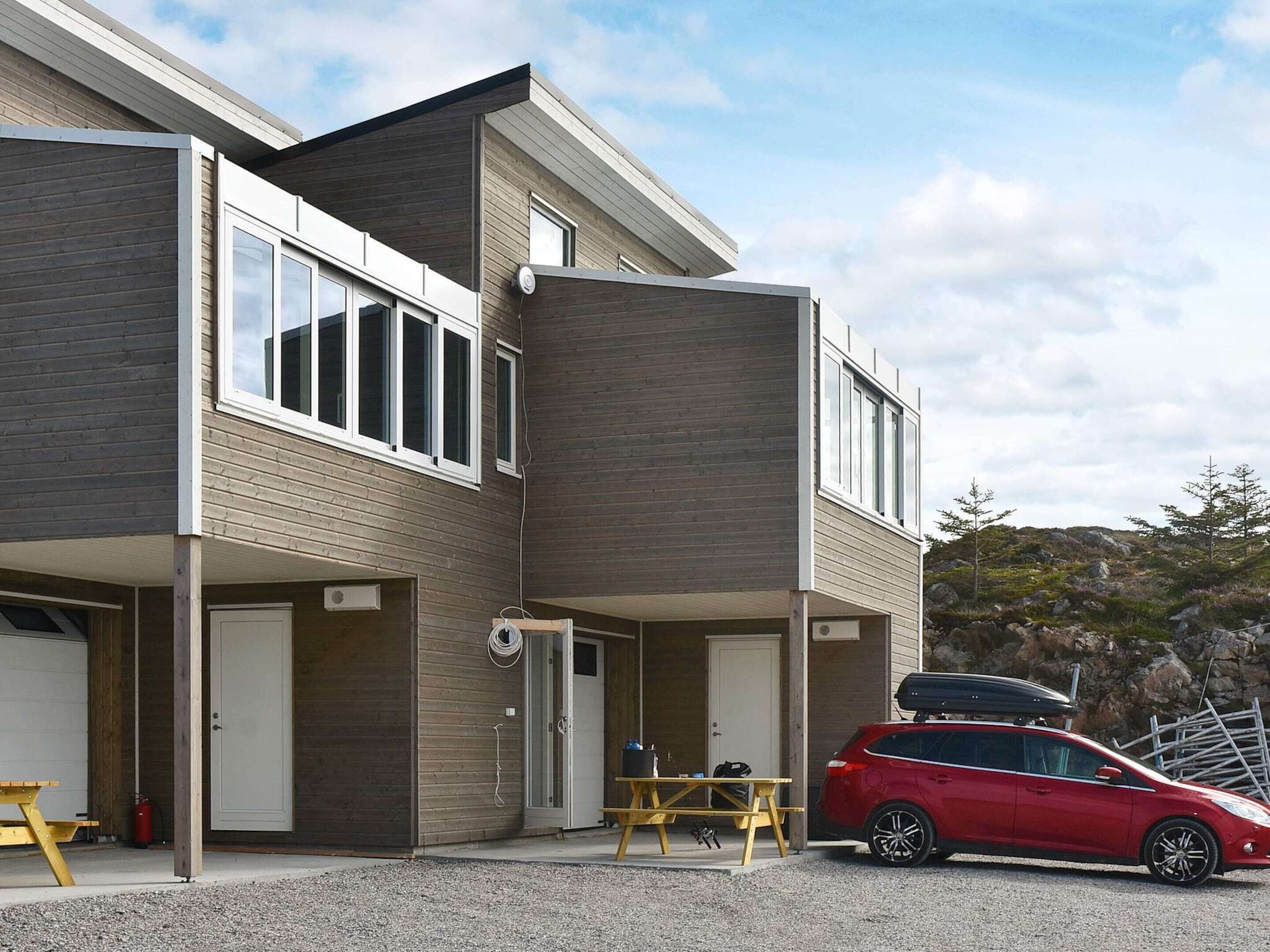 A modern two-story house with a garage, a covered patio, and a red car parked in front.