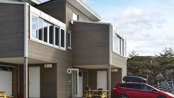 A modern two-story house with a garage, a covered patio, and a red car parked in front.