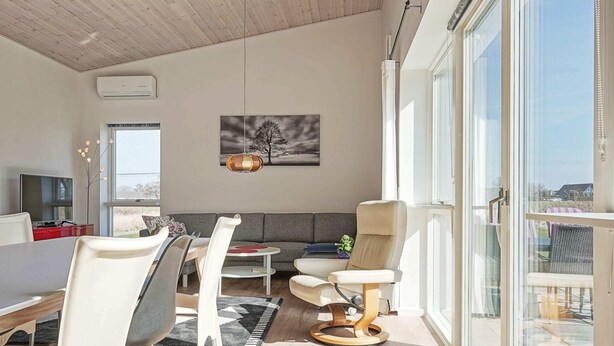 A modern living room with a sofa, chairs, a dining table, and a large window. - 6 Person Holiday Home in Nexo (Nexø)