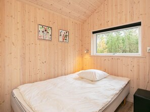 A bedroom with a bed, wooden walls, a window, and two wall-mounted artworks.
