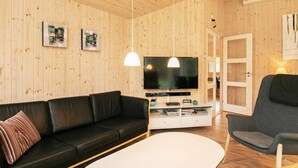 Ett modernt vardagsrum med en svart lädersoffa, ett vitt soffbord och en grå fåtölj. En platt-TV är monterad på väggen, och två hänglampor hänger ovanför.