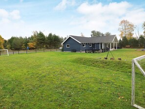 A grassy field with a blue building, a wooden deck, and a soccer goal.