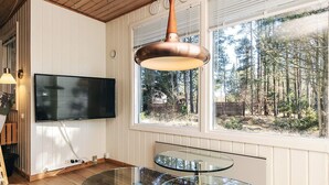 A modern living room with a large TV, a glass coffee table, and a view of a forest through a large window. - 3 Person Holiday Home in Albaek (Aalbaek)