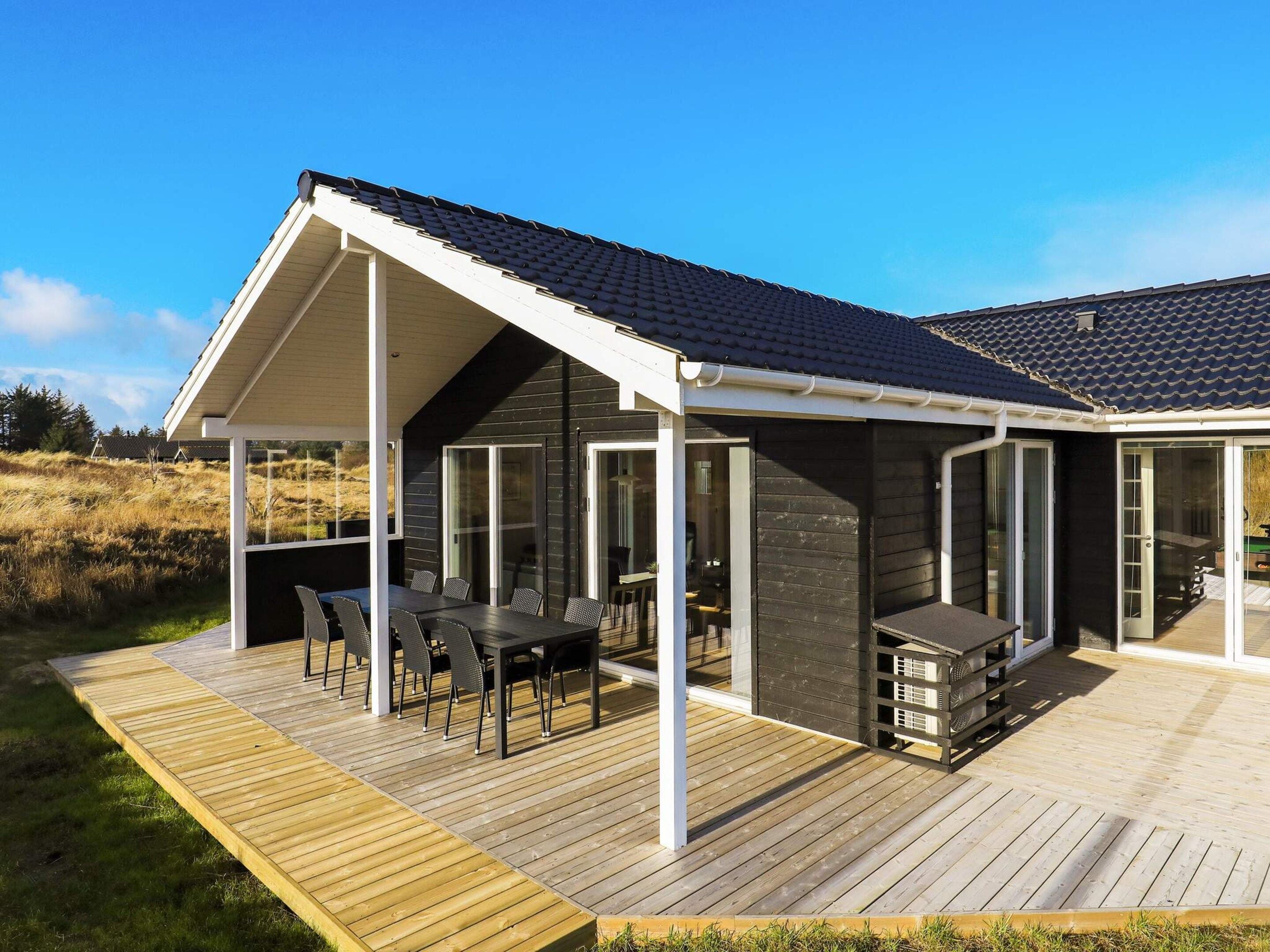 A modern house with a covered patio, a dining area with outdoor furniture, and a large sliding glass door.