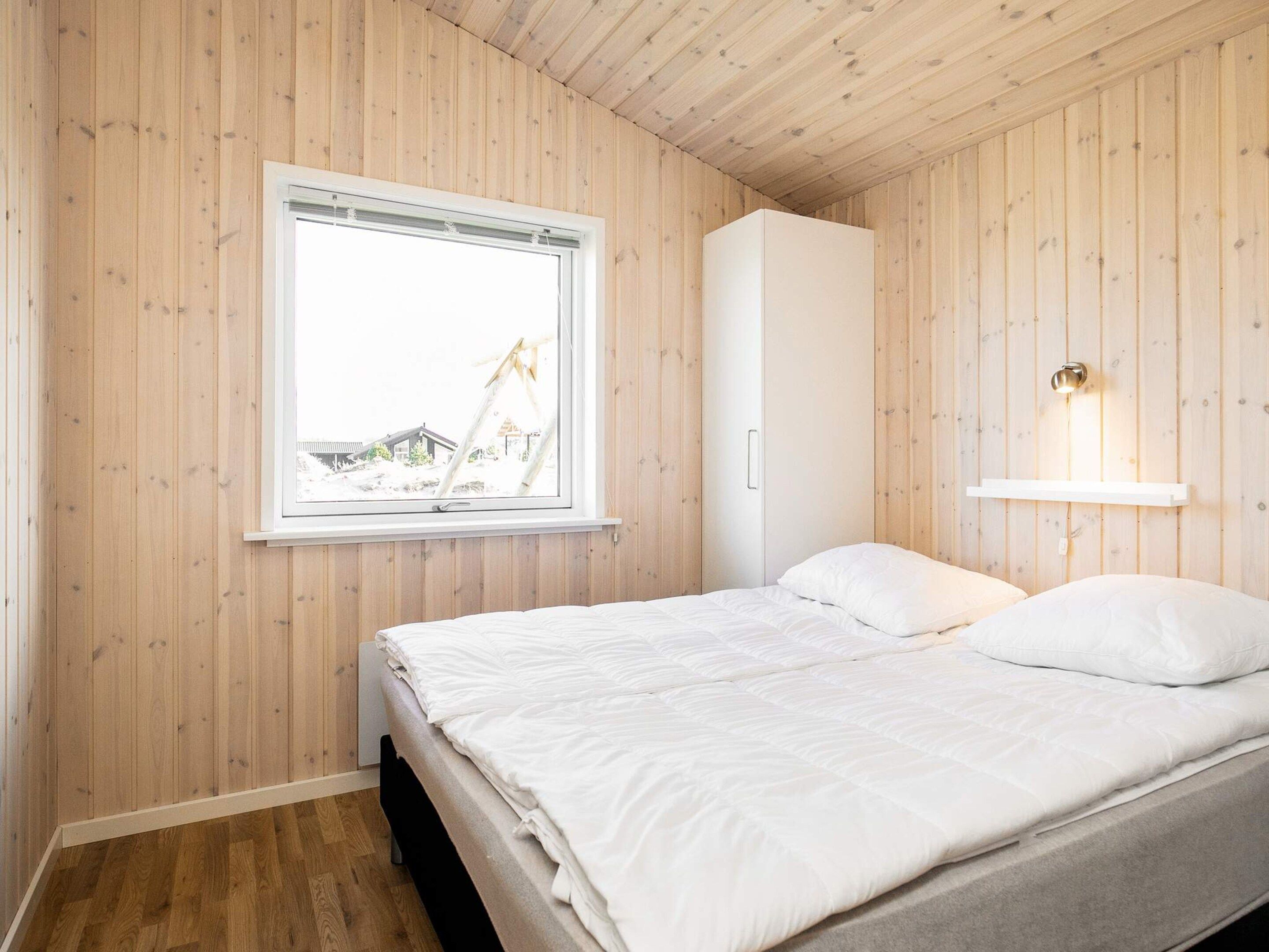 A bedroom with a bed, a window, a wardrobe, and a wall-mounted light fixture.