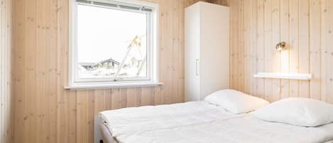 A bedroom with a bed, a window, a wardrobe, and a wall-mounted light fixture.