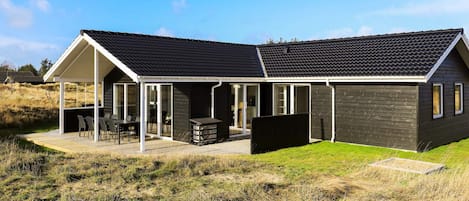 A modern house with a covered patio, a barbecue area, and a large window.