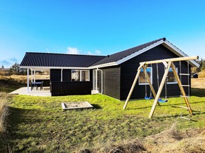 A modern house with a covered patio, a swing set, and a grassy yard.