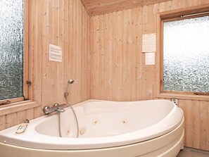 A wooden cabin with a large bathtub, a window with a view, and a wooden door.