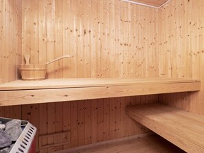 A wooden sauna room with a bench, a wooden bucket with a ladle, and a metal grate.